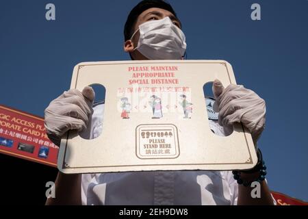 Un employé portant un masque facial comme mesure de précaution contre la propagation du coronavirus, tient un panneau rappelant aux visiteurs de maintenir la distance sociale pendant la réouverture du parc Disneyland de Hong Kong alors que le gouvernement perd les mesures de distance sociale du coronavirus (Covid-19). Banque D'Images