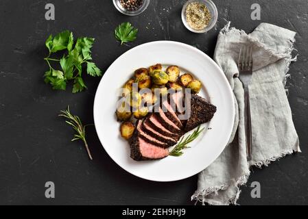 Steak de bœuf grillé avec choux de bruxelles sur plaque sur fond de pierre noire. Vue de dessus, plan d'appartement Banque D'Images