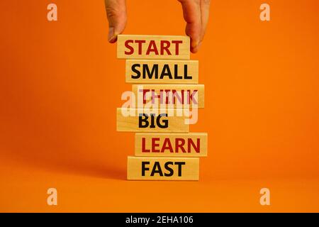 Commencez petit, petit, gros, symbole. Mots « Démarrer petit, penser grand, apprendre vite » sur des blocs de bois sur un magnifique fond orange. Main d'homme d'affaires. Entreprise, Banque D'Images