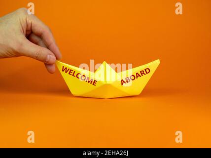 Image d'un homme d'affaires poussant le papier fait le bateau d'origami vers l'avant dans une image conceptuelle. Mots "bienvenue à l'étranger". Sur fond orange avec espace de copie. Unité commerciale Banque D'Images