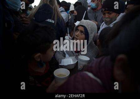 Tijuana, Mexique. 19 février 2021. Un enfant migrant qui vient de recevoir un repas et un verre regarde au milieu d'une foule de personnes espérant entrer aux États-Unis au poste-frontière. Des dizaines de migrants se sont rassemblés à la frontière entre le Mexique et les États-Unis à la suite du changement d'orientation annoncé dans la politique migratoire des États-Unis. Avec la nouvelle réglementation, l'administration du président américain Biden va à l'encontre de la politique d'immigration restrictive de son prédécesseur Trump. Crédit : Stringer/dpa/Alay Live News Banque D'Images