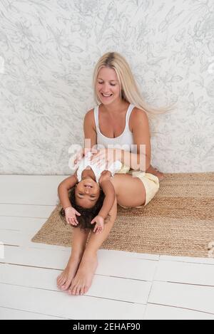 Portrait de la jeune blonde blanche mère tenue joue tickles petite fille afro-américaine dans les bras. La fille rit se trouve sur les jambes de la femme. Tenderne Banque D'Images