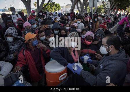 Tijuana, Mexique. 19 février 2021. Une femme portant un masque et des gants en latex remet de la nourriture et de l'eau aux demandeurs d'asile en attente dans le contexte de la pandémie de Corona. Suite à l’annonce d’un changement d’orientation de la politique migratoire des États-Unis, un grand nombre de migrants se sont rassemblés à la frontière entre le Mexique et les États-Unis. Crédit : Stringer/dpa/Alay Live News Banque D'Images