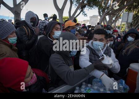 Tijuana, Mexique. 19 février 2021. Un homme portant un masque et des gants en latex distribue de la nourriture et de l'eau aux demandeurs d'asile en attente au passage frontalier « El Chaparral » au milieu de la pandémie de Corona. Suite à l’annonce d’un changement d’orientation de la politique migratoire des États-Unis, un grand nombre de migrants se sont rassemblés à la frontière entre le Mexique et les États-Unis. Crédit : Stringer/dpa/Alay Live News Banque D'Images