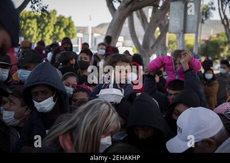 Tijuana, Mexique. 19 février 2021. Les enfants sont portés sur les épaules tandis que de nombreux demandeurs d'asile attendent un repas et un verre au poste frontière « El Chaparral ». Suite à l'annonce du changement d'orientation de la politique migratoire des États-Unis, un grand nombre de migrants se sont rassemblés à la frontière entre le Mexique et les États-Unis dans le contexte de la pandémie de Corona. Crédit : Stringer/dpa/Alay Live News Banque D'Images