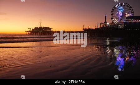 Des vagues de crépuscule contre une grande roue lumineuse classique, parc d'attractions sur la jetée de Santa Monica pacific Ocean Beach Resort. Symbole emblématique de l'été o Banque D'Images