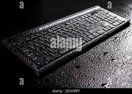 Clavier humide d'un ordinateur personnel. Gouttes d'eau sur un appareil électronique. Arrière-plan sombre. Banque D'Images