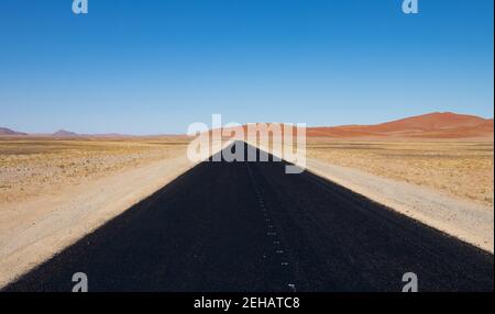 Vue le long d'une route pavée noire de Sesriem à Sossussvlei dans le parc Naukluft, Namibie. Dunes rouges à l'horizon. Banque D'Images