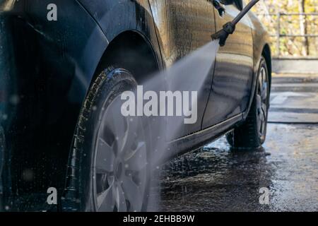 Lavage de voiture à l'extérieur. Lavage de la roue de voiture avec un jet d'eau savonneuse. Activités extérieures et entretien du véhicule. Banque D'Images