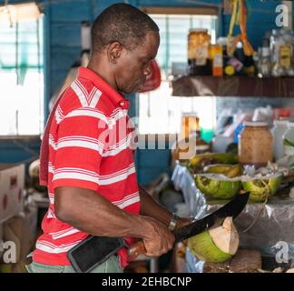 Homme des Bahamas ouvrant une noix de coco pour la vendre à un touriste, Freeport, Bahamas, 2019 Banque D'Images