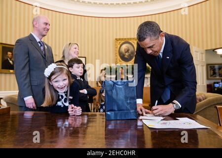 Le président Barack Obama signe des souvenirs pour le mois de mars des dix 2013 l'ambassadrice nationale Nina Centofanti, 8 ans, au bureau de Resolute lors de sa visite au bureau ovale, le 26 mars 2013. Les parents de Centofanti Vince et Christine, le frère Nicholas, et la sœur Mia, non visibles, se tiennent derrière elle. Banque D'Images