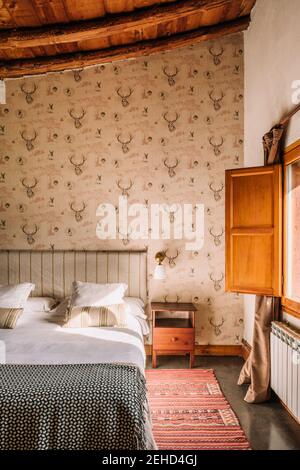 Intérieur d'une chambre élégante avec lit confortable recouvert d'un couvre-lit près de la fenêtre décorée de rideaux Banque D'Images