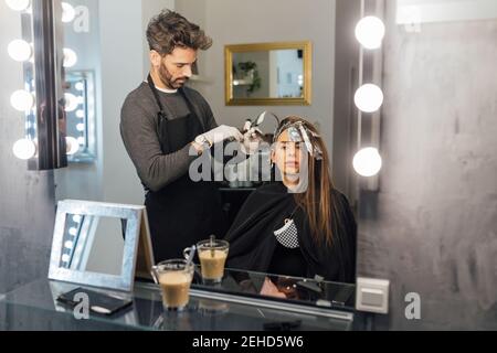 Vue latérale de l'homme ethnique principal focalisé peignant des brins de client féminin avant de teindre en technique de mise en balles Banque D'Images