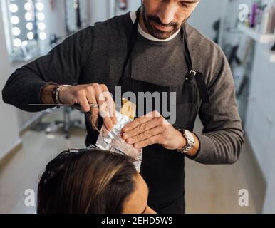 Maître masculin ethnique axé sur la récolte peignant des fils de cliente féminine avant la teinture en technique de balayage Banque D'Images