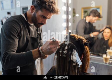 Vue latérale de la culture ethnique masculine maître peignant des brins de la cliente féminine avant la teinture en technique de mise en balles Banque D'Images