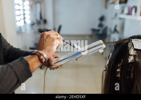 Vue latérale de la récolte de l'homme maître peignant des brins de client féminin méconnaissable avant la teinture en technique de mise en balles Banque D'Images