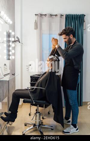 Vue latérale de l'homme ethnique principal focalisé peignant des brins de client féminin avant de teindre en technique de mise en balles Banque D'Images