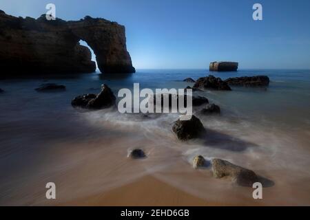 Vue pittoresque des formations rocheuses voûtées sur la côte océanique sous un ciel bleu à Praia da Abandeira, Algarve Portugal Banque D'Images