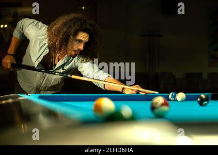 Croiser le mâle barbu focalisé frapper le ballon avec le repère pendant le jeu jeu dans la piscine de billard Banque D'Images