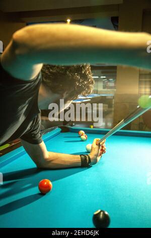 Croiser le mâle barbu focalisé frapper le ballon avec le repère pendant le jeu jeu dans la piscine de billard Banque D'Images