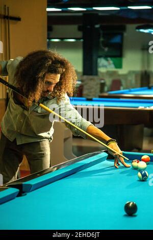 Croiser le mâle barbu focalisé frapper le ballon avec le repère pendant le jeu jeu dans la piscine de billard Banque D'Images