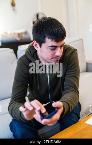 Homme avec un handicap de la vue téléphone mobile défiant tout en étant assis sur canapé à la maison Banque D'Images