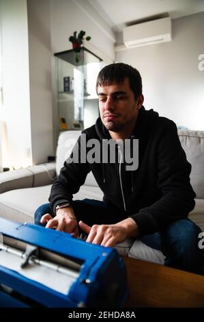 Homme aveugle sérieux assis sur un canapé et écrire sur une machine à écrire avec code système tactile Banque D'Images