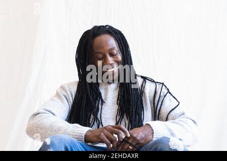 Angle bas d'un homme afro-américain dans des vêtements décontractés assis sur tissu blanc et sourire heureux Banque D'Images