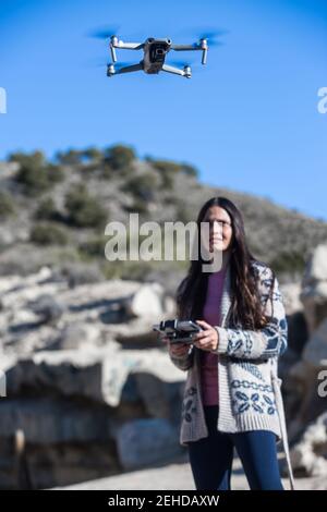 Femme souriante avec télécommande debout dans la nature et en fonctionnement un drone volant au-dessus du sol Banque D'Images