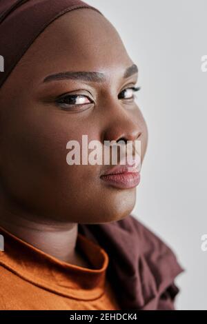 Portrait de la jeune femme noire attrayante dans des vêtements décontractés et turban regardant la caméra Banque D'Images