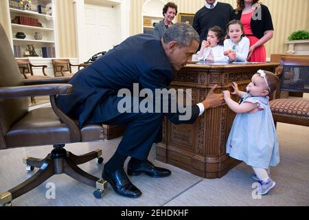 Le président Barack Obama tient la main de Lincoln Rose Pierce Smith, fille de l'ancien secrétaire de presse adjoint Jamie Smith, dans le bureau ovale, le 4 avril 2014. Elsa Smith, âgée de 5 ans, et Sage Smith, âgée de 6 ans, cousins de Lincoln, regardent de l'autre côté du bureau de Resolute. Banque D'Images