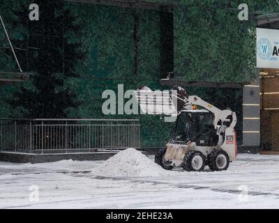 Moscou. Russie. 12 février 2021. Une petite pelle hydraulique avec un godet élimine la neige d'une route dans une rue urbaine lors d'une forte chute de neige. Hiver Banque D'Images