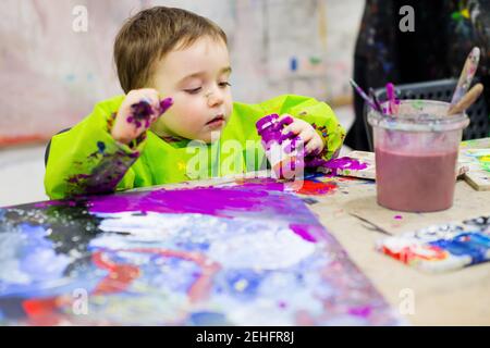 Portrait d'un tout-petit dans une salle de classe d'art tenant une gouache violette peinture Banque D'Images