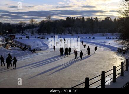 Les patineurs jettent de longues ombres tandis que le soleil se couche sur la patinoire du canal Rideau pendant le bal de neige . Ottawa, Ontario, Canada. Banque D'Images