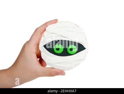 Une jeune femme tient une main avec un biscuit au sucre rond décoré avec du glaçage royal fait maison pour créer une momie à thème d'Halloween. Isolé sur blanc. Banque D'Images