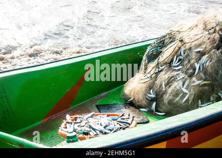 Bateau de pêche avec filet de pêche rempli de poissons et d'océan vagues en arrière-plan Banque D'Images