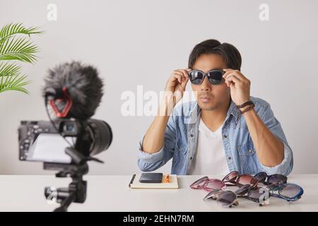 Vlogger asiatique ou Blogger en Jean chemises portent des lunettes de mode noires pour montrer au client tout en enregistrant la vidéo. Freelance Online Streaming avec Custo Banque D'Images