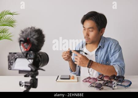 Avant gauche de l'asiatique vlogger ou Blogger dans Jean chemises examen mode lunettes par enregistrement vidéo. Freelance Online Streaming avec le client via Socia Banque D'Images