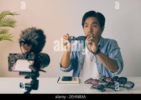 Vlogger asiatique ou Blogger en Jean chemises montrer Black Fashion lunettes pendant l'enregistrement vidéo. Freelance Online Streaming avec le client via social Me Banque D'Images
