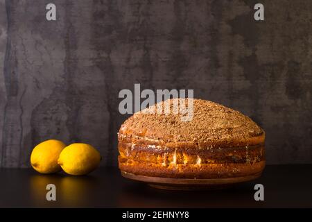 Gâteau au citron parsemé de chocolat râpé avec des citrons sur fond sombre vintage. Le concept de la fabrication du dessert. Banque D'Images