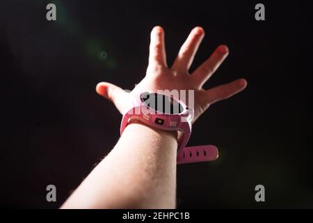 Main enfant avec montre intelligente demandant de l'aide, isolée sur fond noir. Banque D'Images