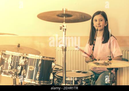 Bonne fille en musicothérapie en jouant au kit de batterie dans la salle de musique. Belle jeune fille batteur avec des pilons jouant des tambours et des cymbales. Batteur féminin Banque D'Images