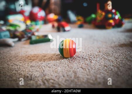 Image de faible profondeur de champ (mise au point sélective) avec une boule de caoutchouc colorée sur le sol de la chambre d'un enfant, avec des jouets en arrière-plan. Banque D'Images