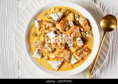 Cuisine allemande : ragoût de porc à la crème, cornichons et fromage bleu, paprika fumé servi sur une assiette blanche avec une cuillère dorée sur un dos en bois blanc Banque D'Images