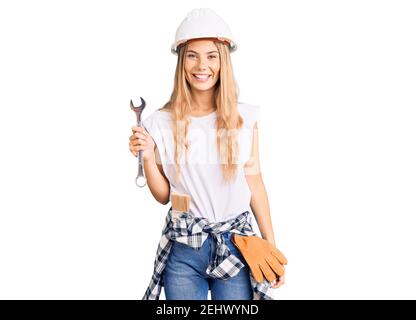 Belle femme caucasienne avec cheveux blonds portant un casque et un constructeur vêtements ayant l'air positif et heureux debout et souriant avec un sourire confiant Banque D'Images