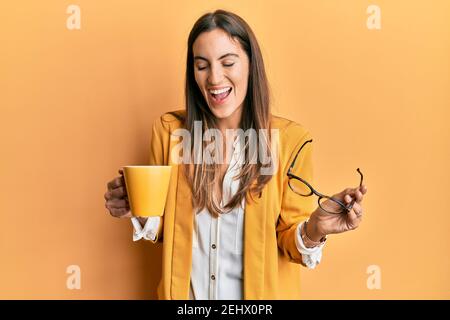 Jeune belle femme portant un style d'affaires buvant une tasse de café souriant et riant fort parce que drôle de blague folle. Banque D'Images