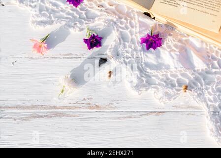 Fleurs violettes sur un livre. Nappe ajourée tricotée sur une vieille table en bois. Soirée dans le village. Coucher de soleil à l'extérieur, batanica, belles fleurs Banque D'Images