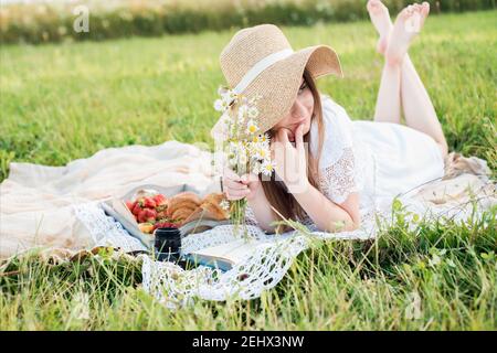 Fille dans un champ avec des pâquerettes, l'été dans le village.jeune femme souriante se relaxant à l'extérieur et ayant un pique-nique, elle est couchée sur une couverture sur le Banque D'Images