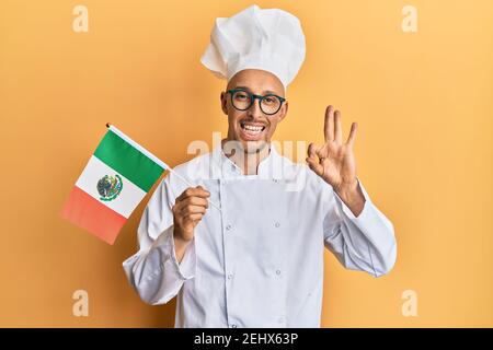 Homme chauve avec barbe portant un tablier de cuisinier professionnel tenant le drapeau du mexique faisant signe ok avec les doigts, souriant sympathique gestante excellent symbole Banque D'Images