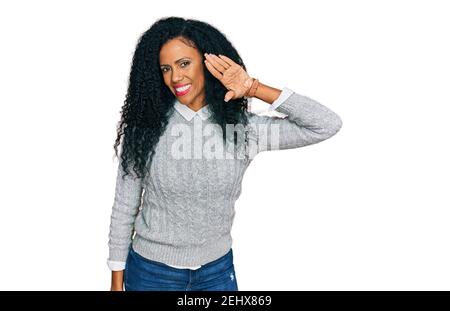 Femme afro-américaine d'âge moyen vêtue de vêtements décontractés en disant bonjour heureux et souriant, geste de bienvenue amical Banque D'Images